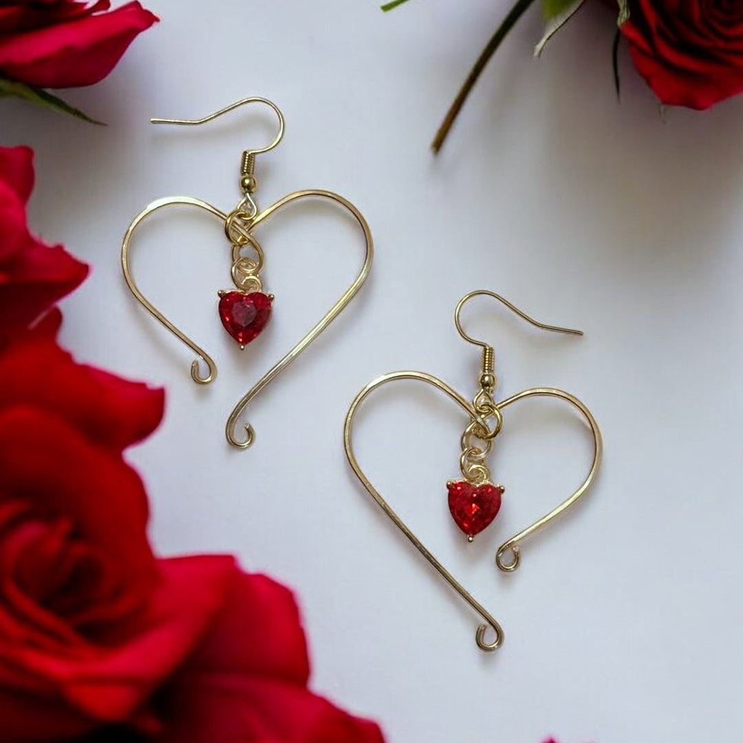 Heart-shaped gold earrings with red stones on a white background with red roses.