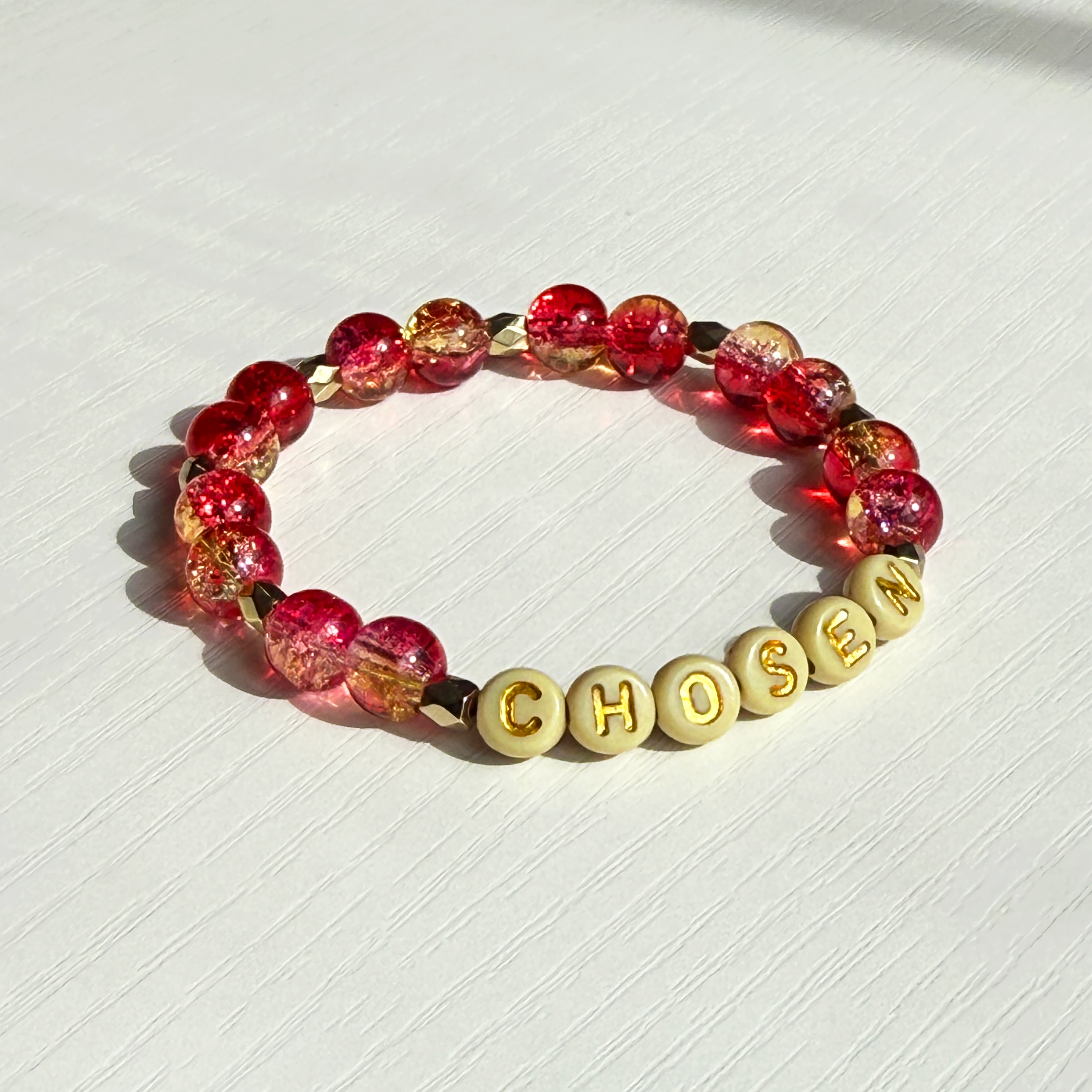 Bracelet with red and gold beads and 'CHosen' letters on a white background