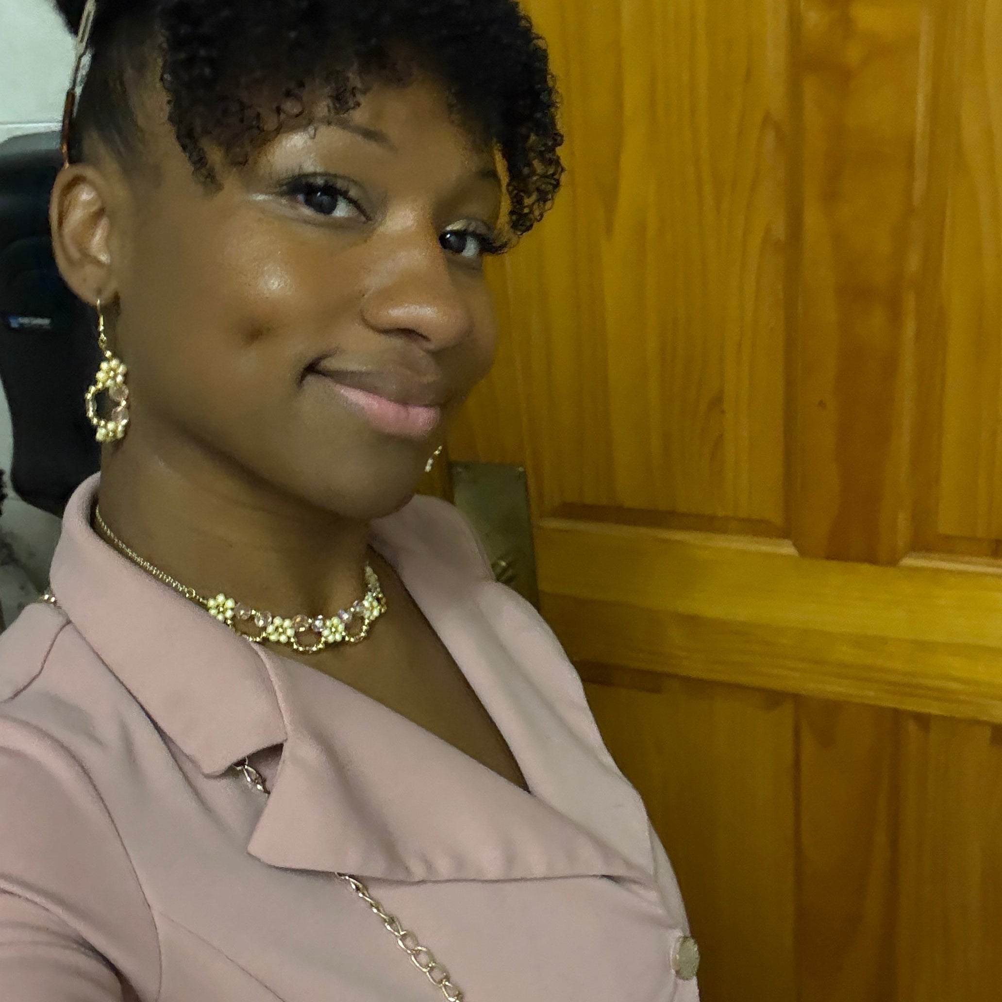 Woman wearing a beige outfit with a necklace in front of a wooden door.