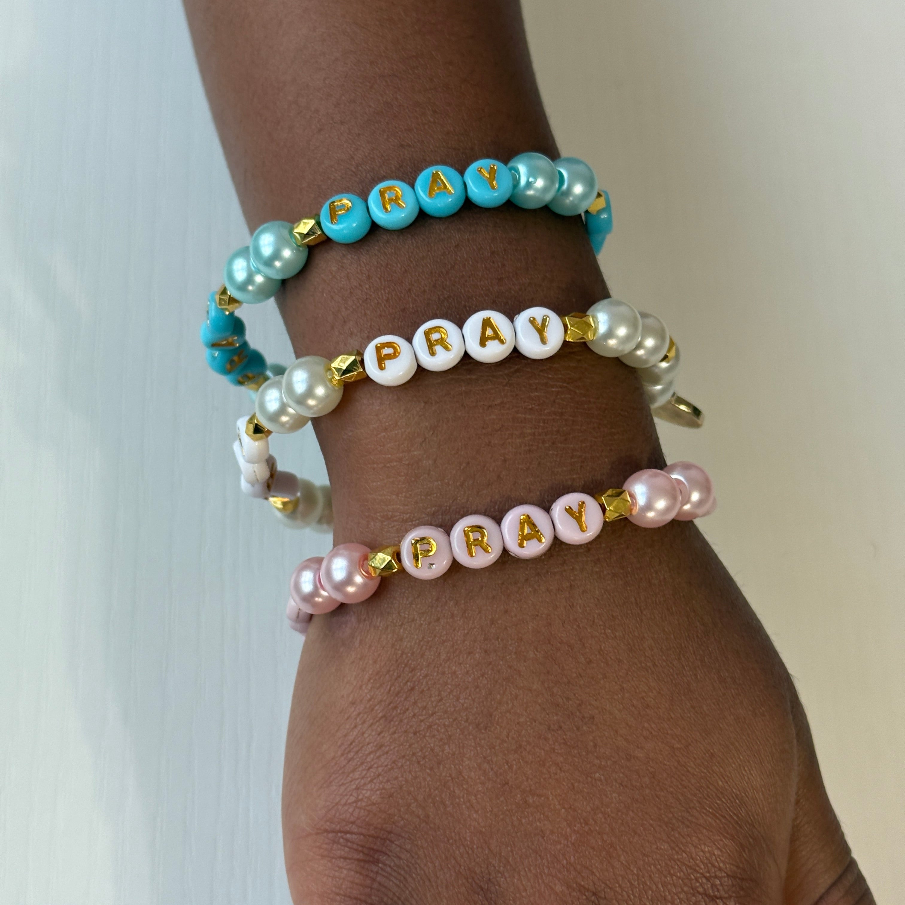 Three beaded bracelets with 'PRAY' on a wrist against a neutral background