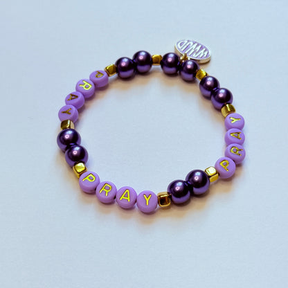 Purple beaded bracelet with 'PRAY' on a light blue background