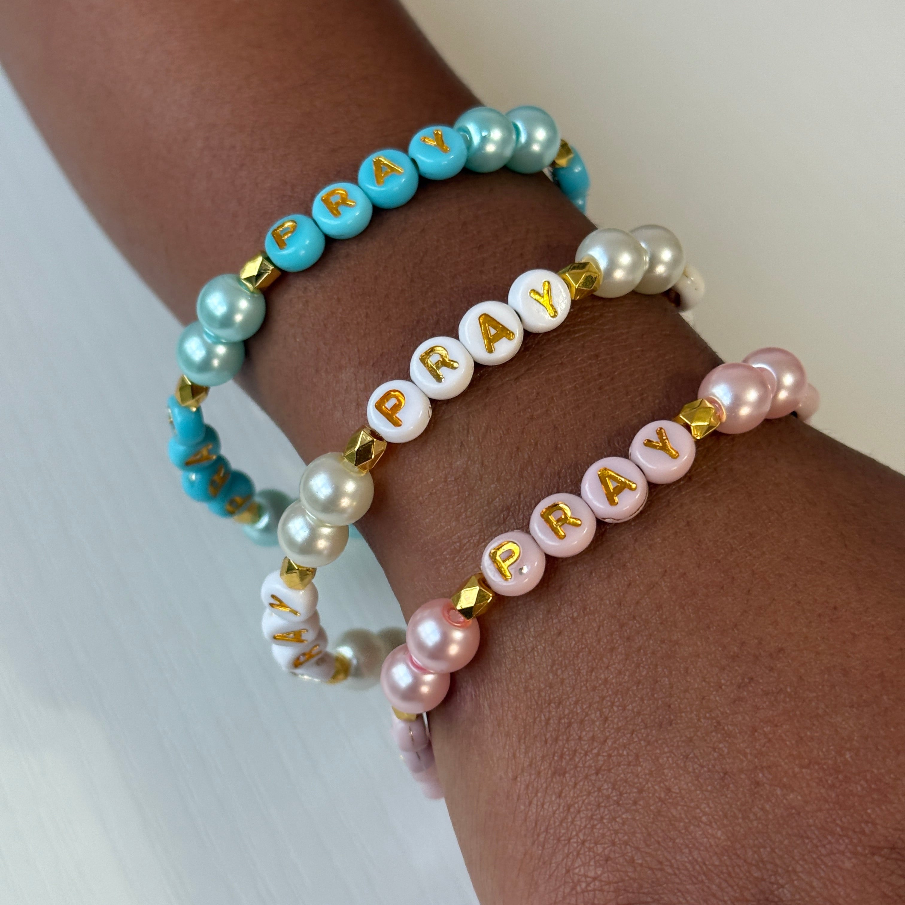 Three beaded bracelets with 'PRAY' on a wrist against a white background