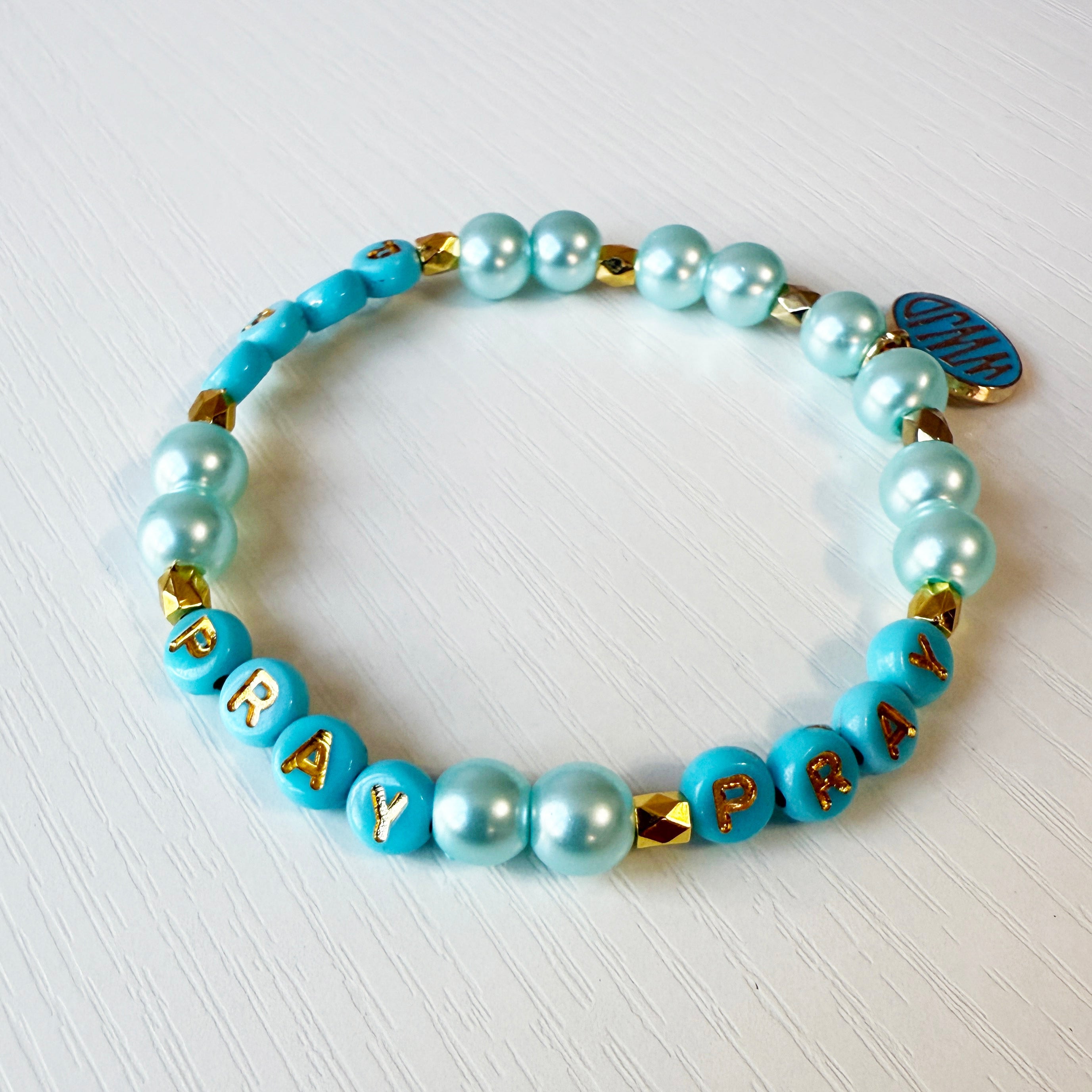 Turquoise beaded bracelet with 'PRAY' pattern on a white background