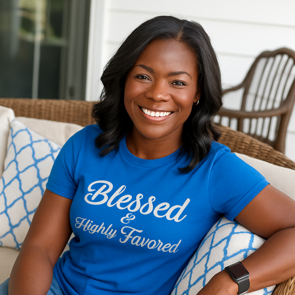 Woman wearing a blue t-shirt with 'Blessed & Highly Favored' text, sitting on a couch.