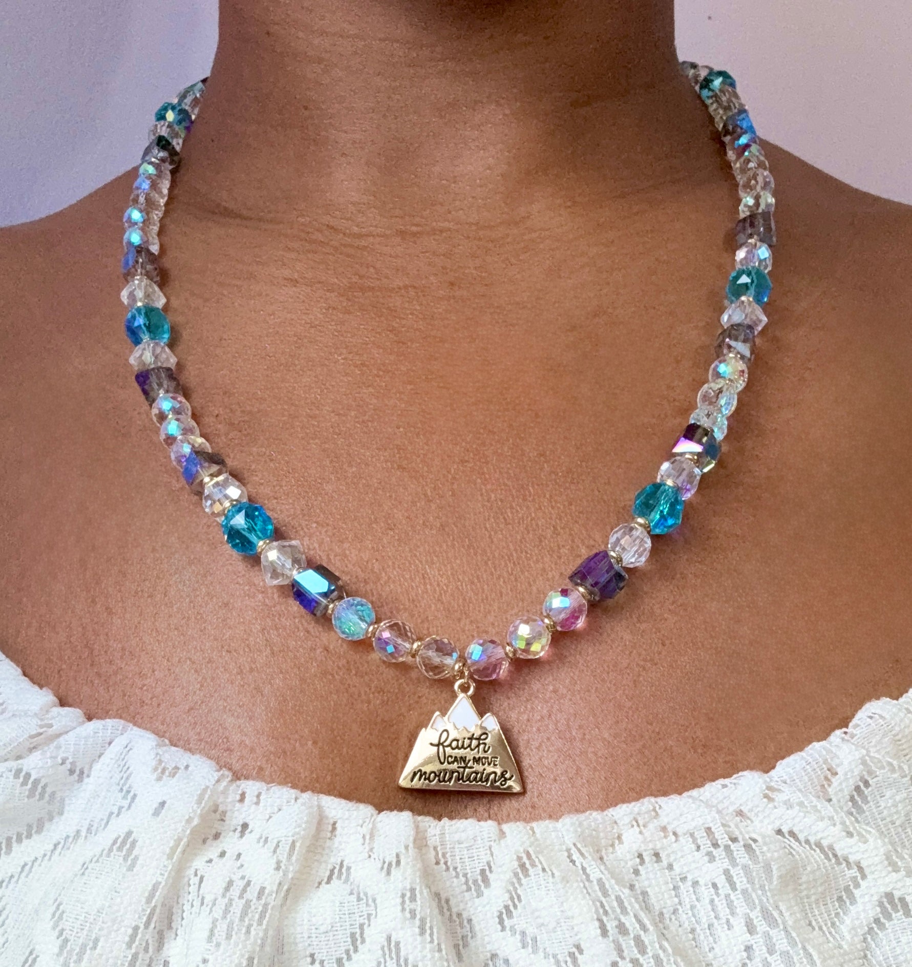 Necklace with multicolored beads and a triangle pendant on a person wearing a white lace top.