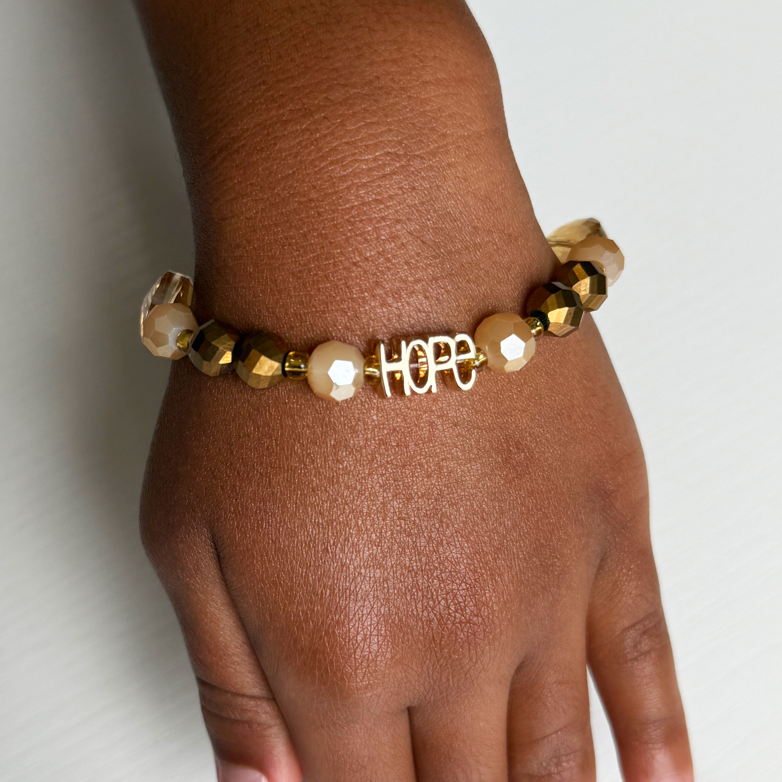 Gold and pearl beaded bracelet with 'HOPE' charm on a wrist against a light background