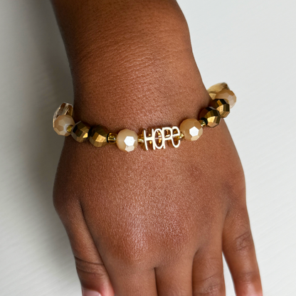 Gold and pearl beaded bracelet with 'HOPE' charm on a wrist against a light background